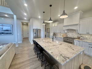 Kitchen with light stone countertops, a breakfast bar, tasteful backsplash, and white cabinets