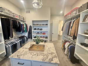 Walk in closet with dark colored carpet and hanging lights