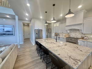 Kitchen featuring a large island, light stone counters, a kitchen bar, white cabinetry, and premium appliances