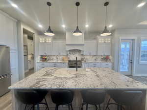 Kitchen with glass insert cabinets, light stone counters, a breakfast bar area, and light wood-style flooring