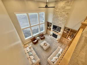 Living room with a fireplace, a high ceiling, ceiling fan, and built in features