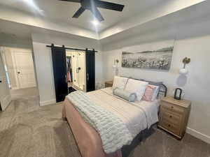 Bedroom featuring a barn door, a raised ceiling, dark colored carpet, a spacious closet, and a ceiling fan