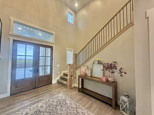 Foyer entrance with french doors, light wood-type flooring, and a high ceiling