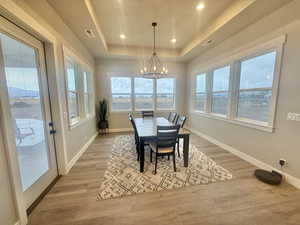 Dining area with a chandelier, light wood-style flooring, and a raised ceiling