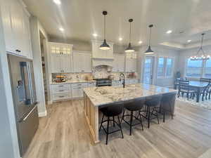 Dual tone kitchen featuring glass fronted cabinets, high quality appliances, light stone countertops, a kitchen breakfast bar, and a spacious island