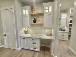Bar featuring white cabinetry, light stone counters, and light wood-type flooring