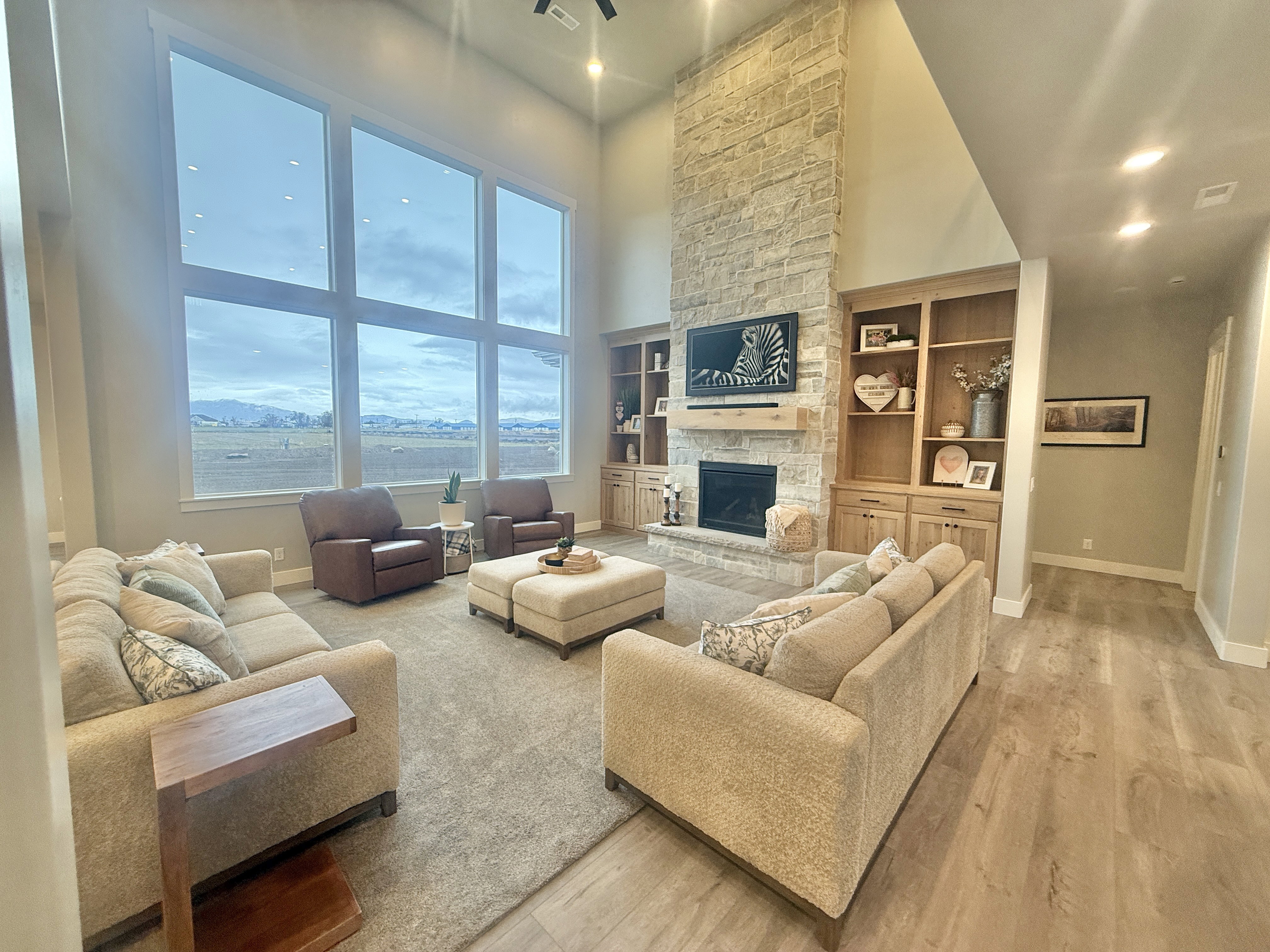 Living area featuring a high ceiling, recessed lighting, a stone fireplace, light wood-type flooring, and built in shelves