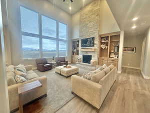 Living area featuring a high ceiling, recessed lighting, a stone fireplace, light wood-type flooring, and built in shelves