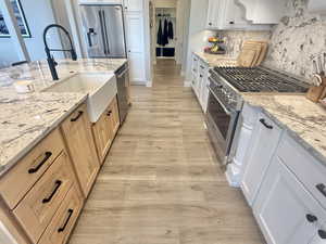 Kitchen featuring light wood-style flooring, stainless steel appliances, light stone countertops, decorative backsplash, and two tone cabinets