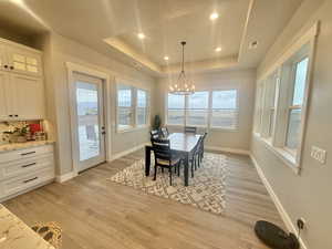 Dining area featuring a chandelier, light wood-style floors, plenty of natural light, and a tray ceiling