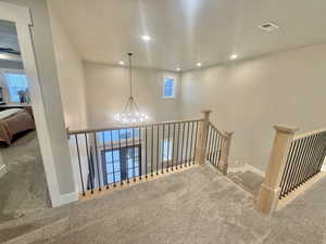 Hall featuring carpet floors, a chandelier, and an upstairs landing