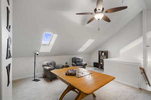 Loft featuring a skylight, lofted ceiling, light colored carpet, and ceiling fan