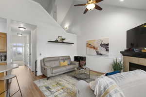 Living room with a fireplace, light wood finished floors, a ceiling fan, a wainscoted wall, and a high ceiling