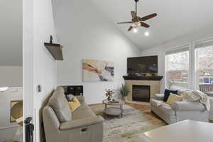 Living room featuring a fireplace, wood finished floors, ceiling fan, wainscoting, and lofted ceiling