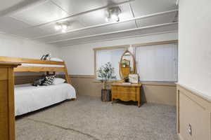 Bedroom featuring wainscoting, light carpet, and a decorative wall