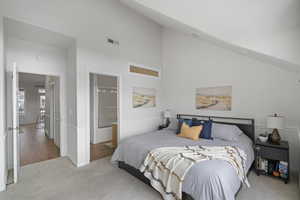 Primary Bedroom featuring light colored carpet, vaulted ceiling, and ensuite bathroom