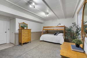 Bedroom with light colored carpet, a wainscoted wall, and a decorative wall