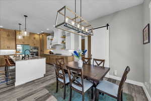 Dining space with a barn door, dark wood-style flooring, and suspended lighting