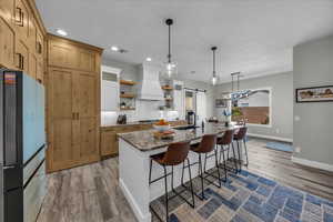 Dual tone kitchen with dark stone counters, light wood-type flooring, open shelves, a breakfast bar area, and an island with sink