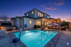 Back of house at dusk featuring outdoor furniture, a hot tub, a patio, and stucco siding