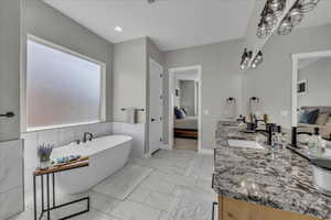 Ensuite bathroom featuring double vanity, a freestanding tub, wainscoting, and light marble finish floors