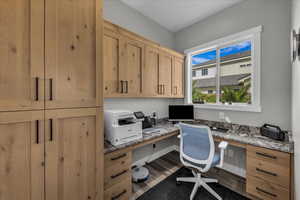 Home office with built in desk and dark wood-style flooring