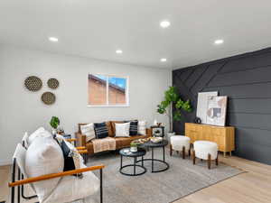 Living room with wood finished floors, an accent wall, recessed lighting, and a decorative wall