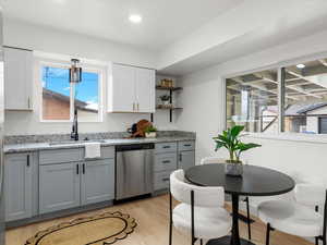 Kitchen with light stone counters, dishwasher, light wood-type flooring, gray cabinetry, and open shelves