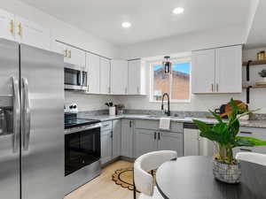 Two tone kitchen with stainless steel appliances, two tone cabinets, light stone countertops, light wood-style floors, and recessed lighting