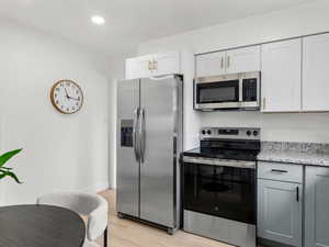 Kitchen featuring stainless steel appliances, light wood finished floors, light stone counters, white cabinetry, and recessed lighting