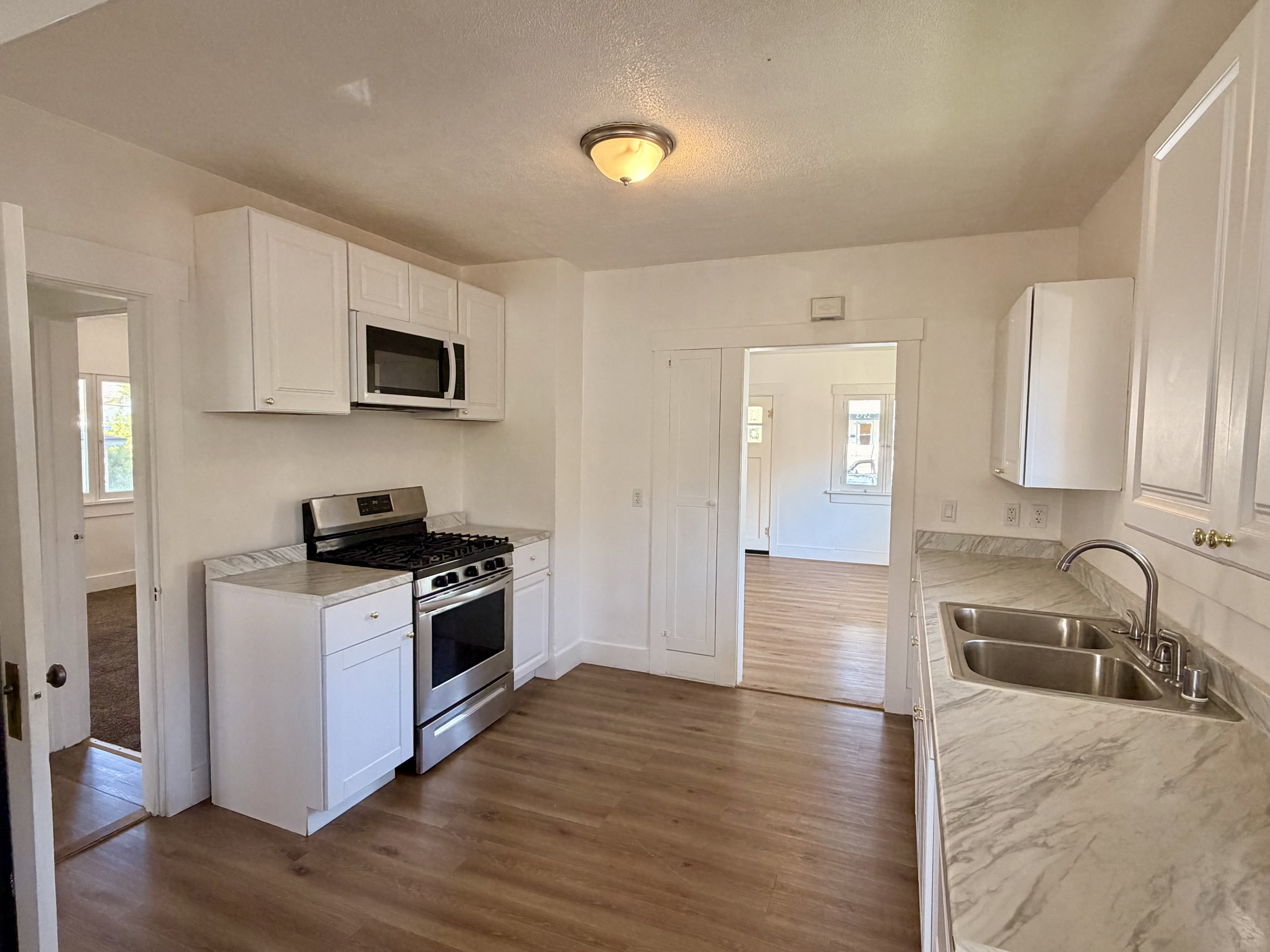 Kitchen with white cabinetry, stainless steel range, built-in microwave, dual basin sink, and wood-finish flooring