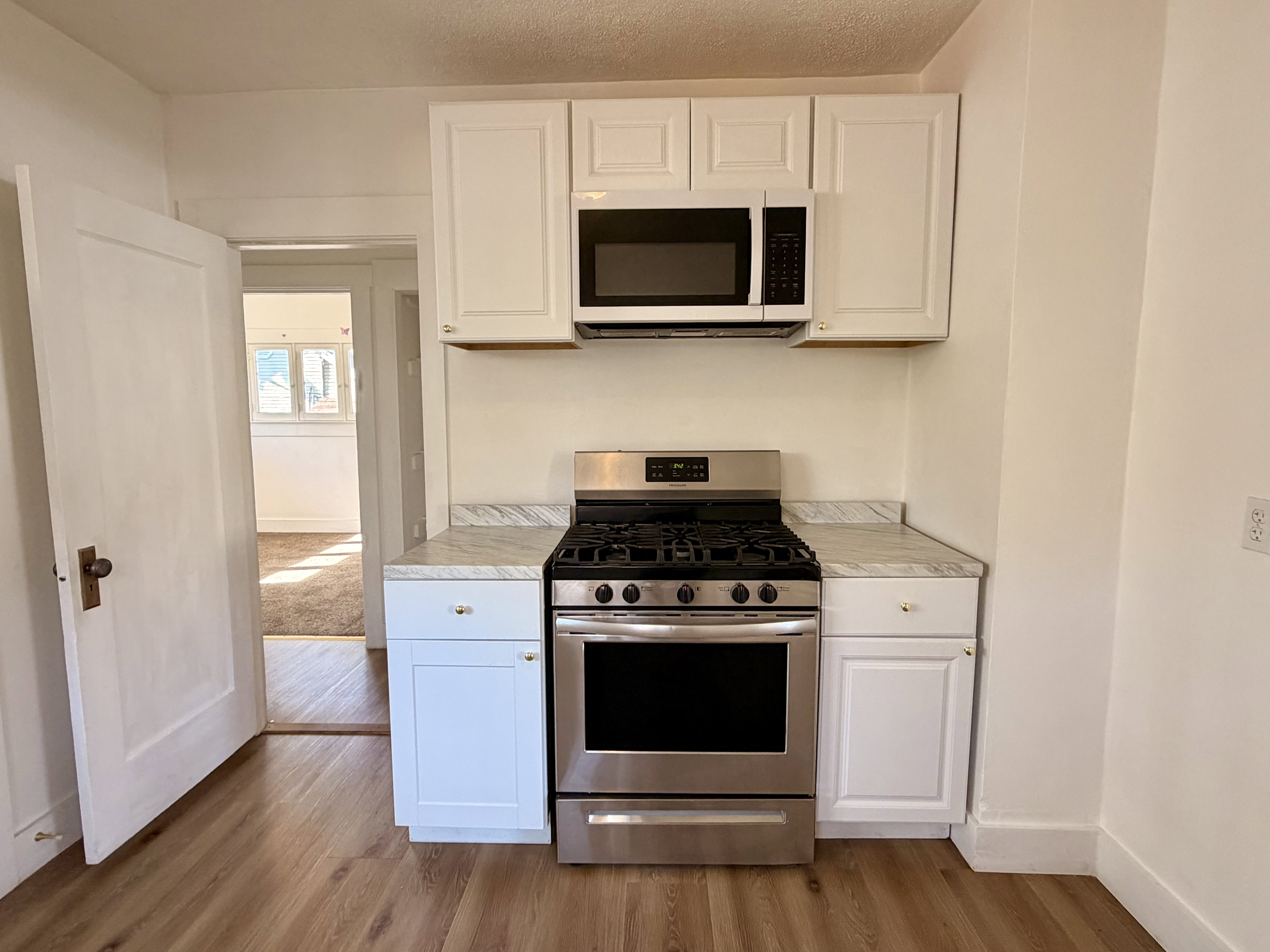 Kitchen featuring white cabinetry with brushed nickel hardware, stainless steel gas range, coordinating stainless steel microwave, and light-toned countertops