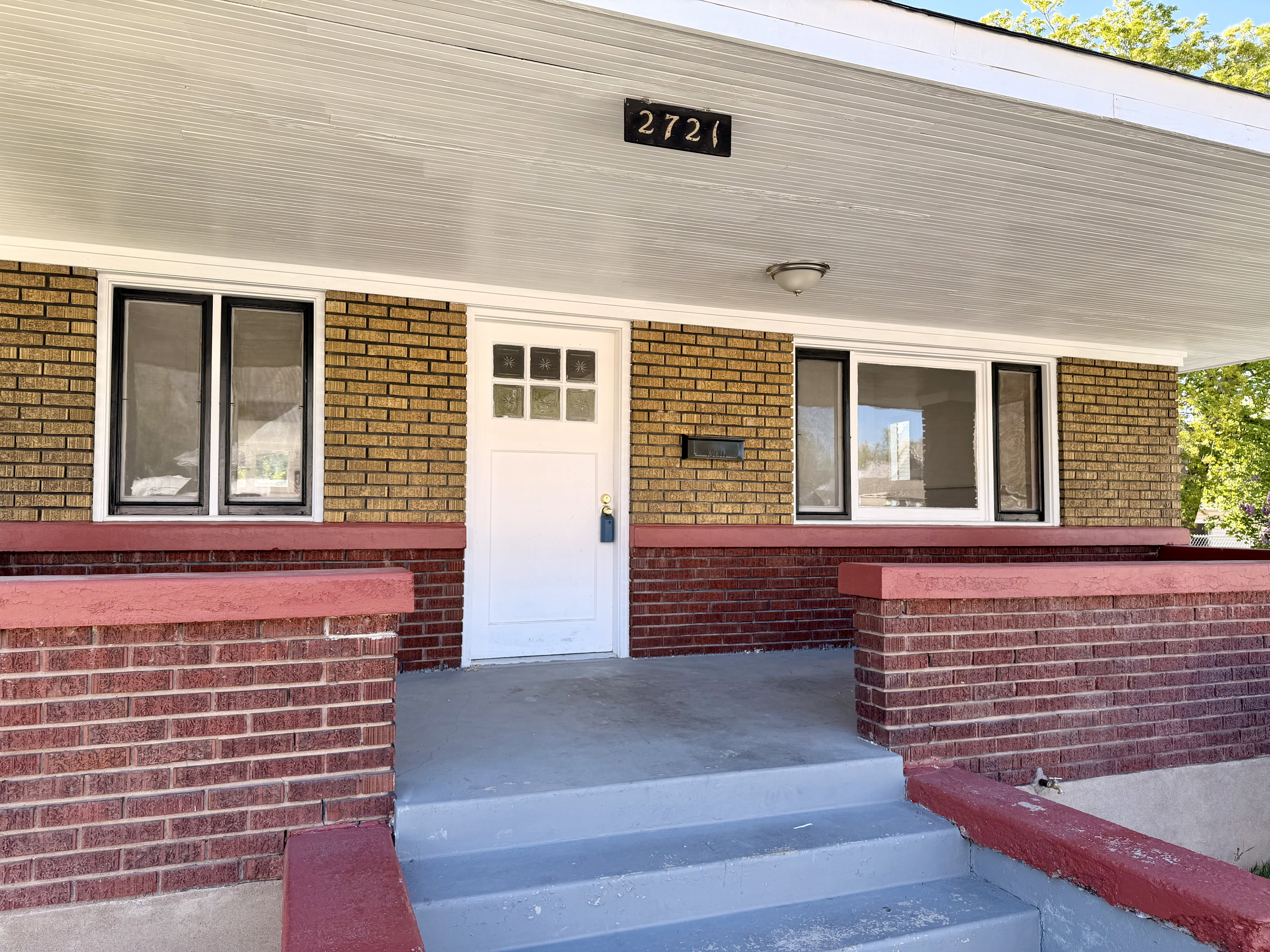 Inviting front porch featuring a white entry door with divided lites, two windows with black framing, brick veneer siding, and a covered ceiling