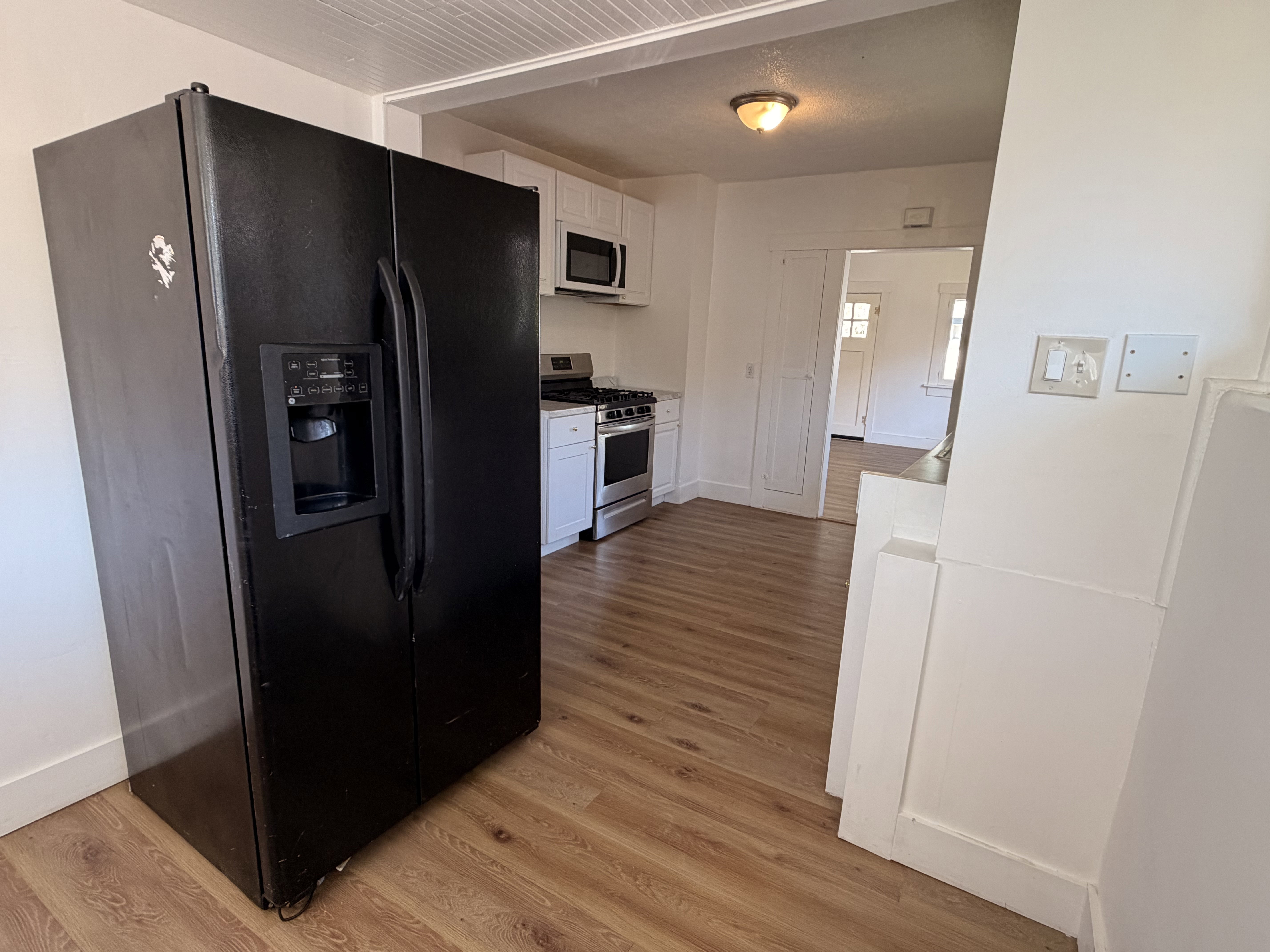 Kitchen featuring a black side-by-side refrigerator with ice and water dispenser, wood-finish flooring, white cabinetry, a stainless steel range, and a built-in microwave