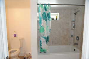 Full bathroom with toilet and shower / bath combination with curtain