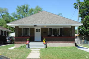 View of front of home with brick siding, covered porch, roof with shingles, and a front lawn