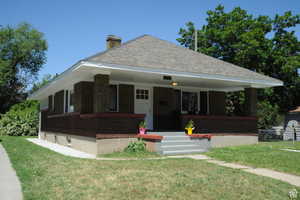 Bungalow-style home featuring a porch, a front yard, brick siding, a chimney, and a shingled roof