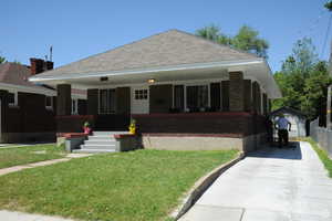 Bungalow-style house with a front yard, covered porch, an outbuilding, and brick siding