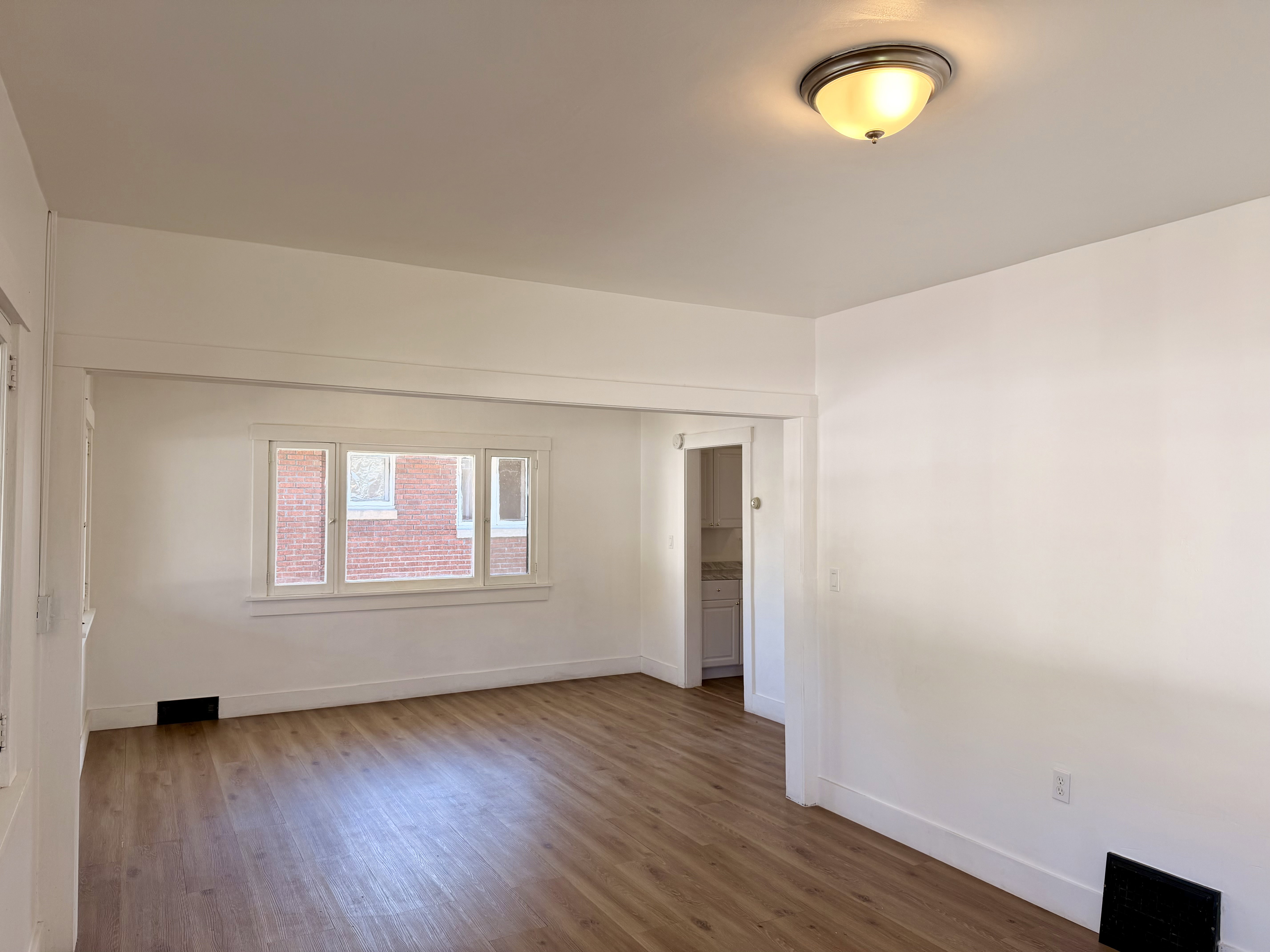 Bright living area featuring wood-finish flooring, white baseboards, and a multi-pane window with white trim