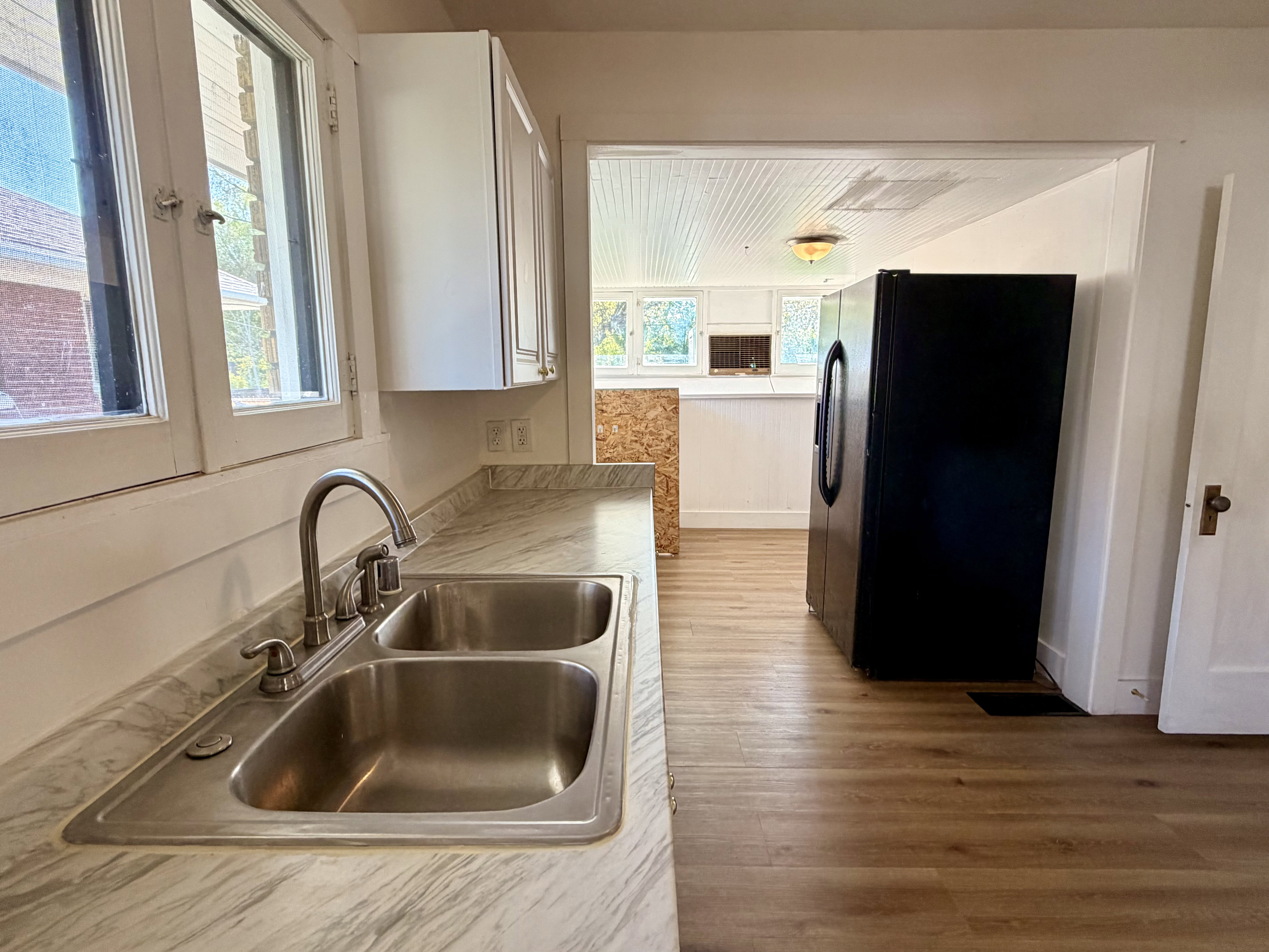 Kitchen featuring a double basin stainless steel sink, light-toned countertop, white cabinetry, and wood-finish flooring