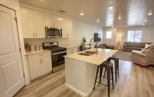 Kitchen with open floor plan, stainless steel appliances, an island with sink, white cabinets, and light wood-style floors