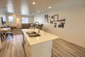 Kitchen featuring open floor plan, a center island with sink, light wood-style floors, recessed lighting, and white cabinets