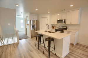 Kitchen featuring stainless steel appliances, a breakfast bar area, white cabinets, a center island with sink, and light wood-style floors