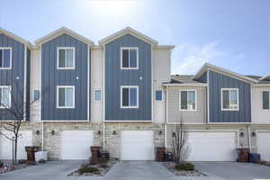 View of front of property featuring board and batten siding, an attached garage, driveway, and stone siding