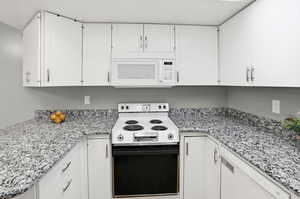 Kitchen featuring white appliances, white cabinets, and light stone counters