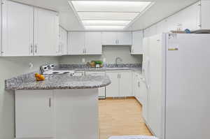 Kitchen featuring white appliances, white cabinetry, a peninsula, and light wood-type flooring