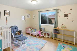 Bedroom with a crib, light wood-style flooring, and a textured ceiling