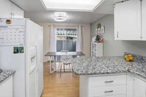 Kitchen featuring white refrigerator with ice dispenser, white cabinets, light stone countertops, and a textured ceiling