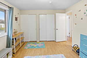 Bedroom with multiple closets, light wood-type flooring, and a textured ceiling