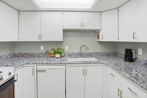 Kitchen with white dishwasher, white cabinetry, and light stone counters
